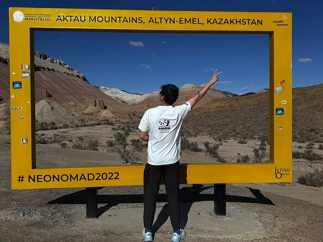Une personne debout devant un panneau jaune encadrant le paysage des monts Aktau.