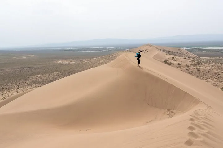 Une personne marche le long de la crête acérée d’une grande dune de sable et prend des photos.