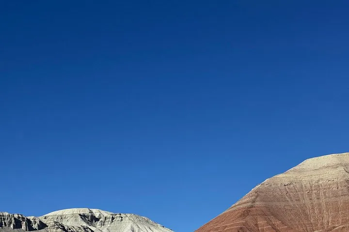 Die Spitze farbenfroher, geschichteter Berge vor einem klaren, tiefblauen Himmel.